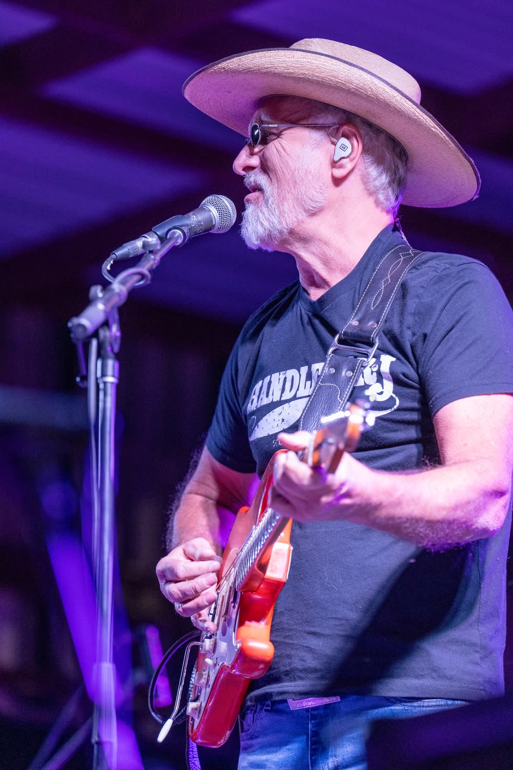 A bass player under purple light with a fan's hand raised at the edge of the stage.