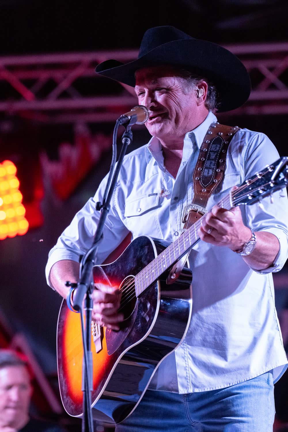 Tracy Byrd singing at the microphone in a black cowboy hat, guitar in hand, on the Coyote stage.