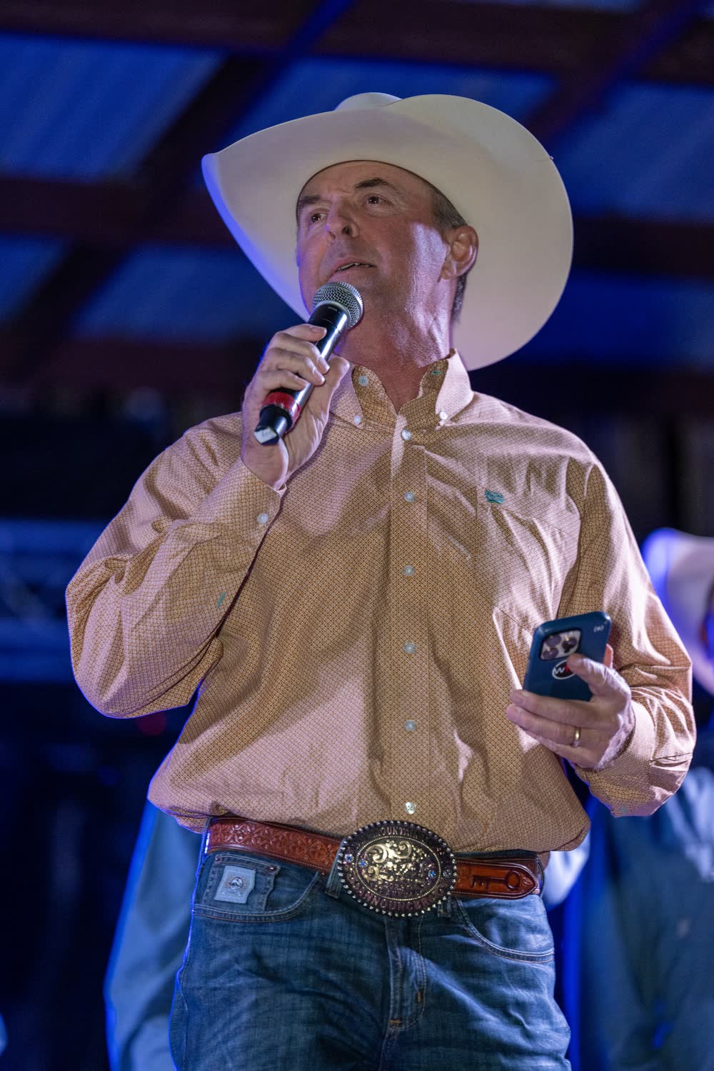 An emcee in a white cowboy hat speaking into the microphone on the Coyote stage.