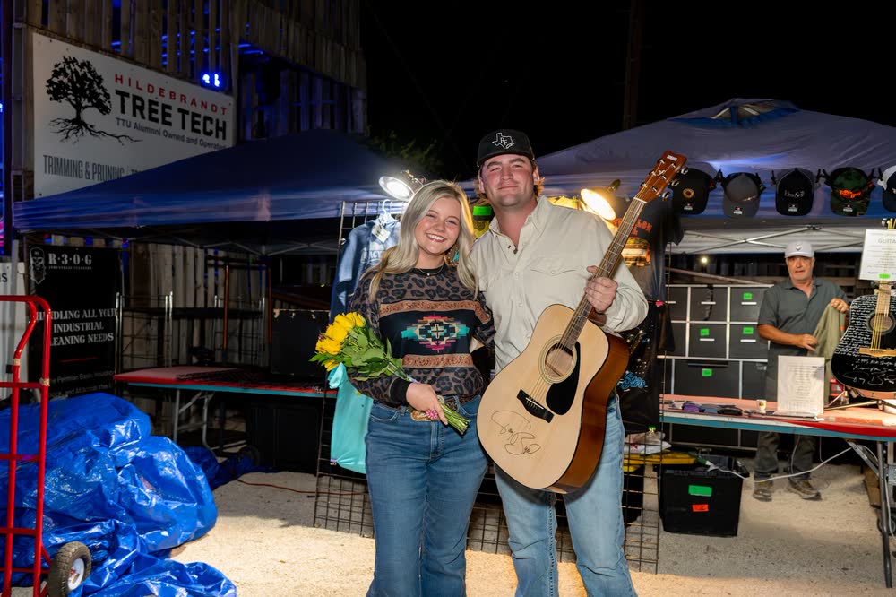 A couple on stage holding a signed guitar they won at the show.