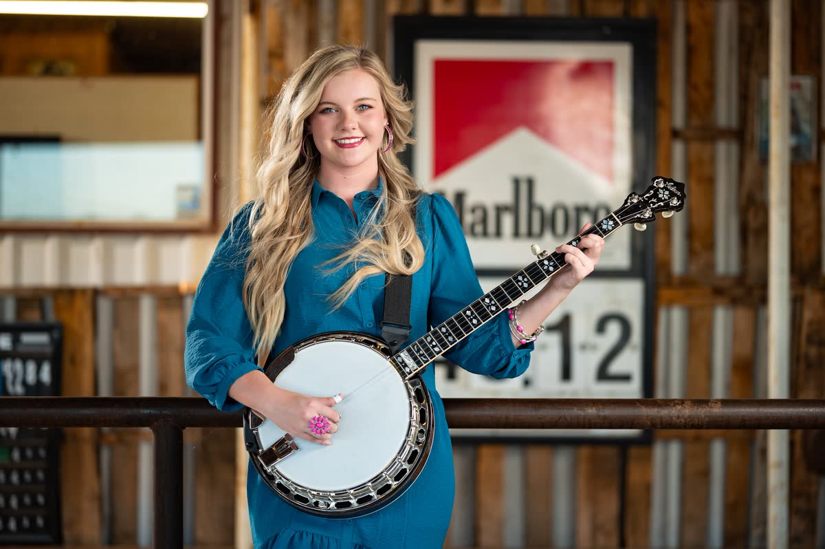 Hadlie Jo smiling with her banjo, the Marlboro sign on the wall of The Coyote Store behind her.