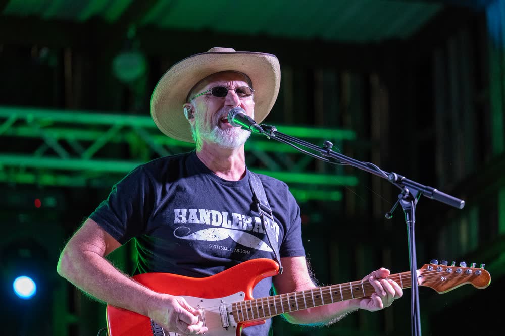 A guitarist in a straw cowboy hat singing under green stage light.