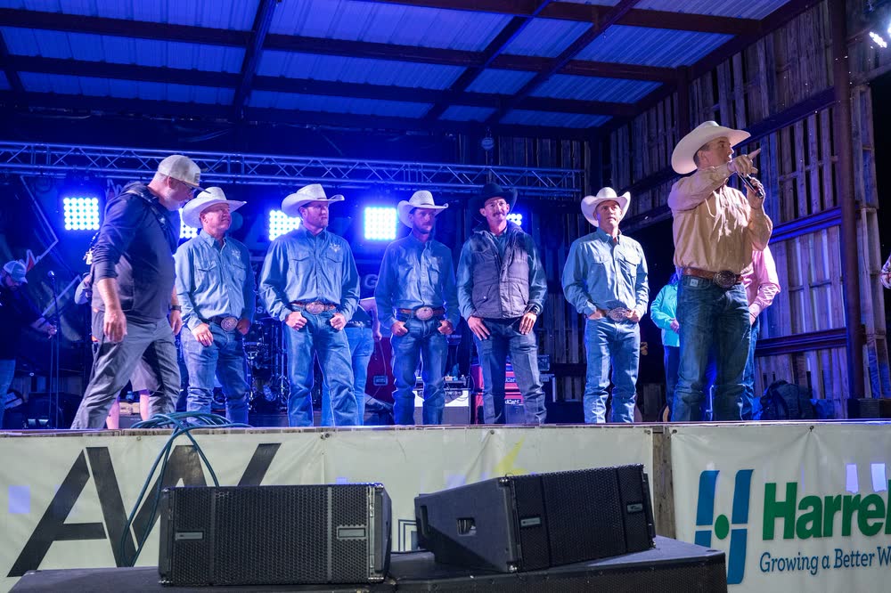 A line of men in cowboy hats standing across the Coyote stage under blue light.