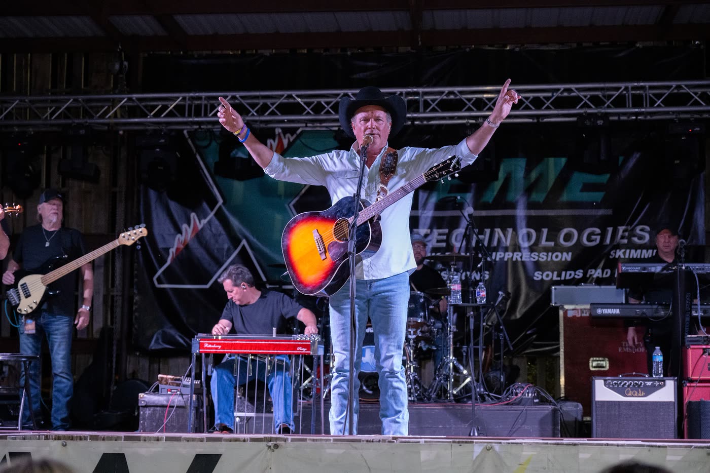 A singer with arms spread wide on the Coyote stage, full band behind him and the crowd's hands up front.