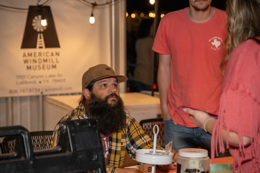 A bearded vendor under the string lights at a booth beside the Coyote Store.